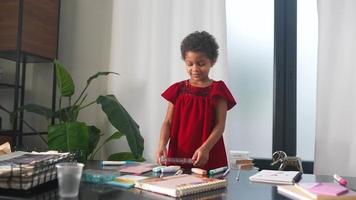 Young girl in red dress plays with markers at a table drawing in notebook video