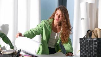 Young woman looks at large piece of paper with pencil in hand before looking at camera video