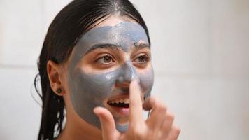 mujer joven con el pelo mojado aplica máscara de arcilla a la cara