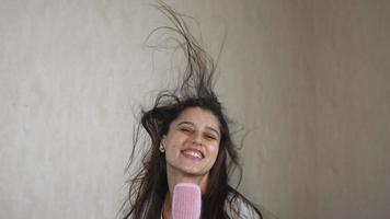 Woman blow drying hair jumps up and down singing into pink hair brush in slow motion video