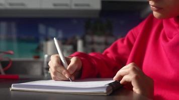 Close up of a young woman taking notes in a notebook with a pen