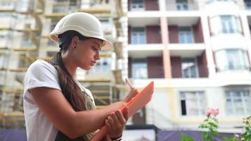 mujer con sombrero duro blanco en zona de construcción piensa y toma notas en papel video