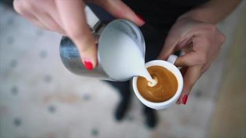 dichtbij omhoog van barista handen met rood nagels gieten gestoomd melk in een kop van espresso schoten voor latte kunst video