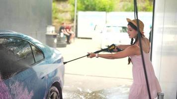 Young woman in pink dress and straw hat washes a car video