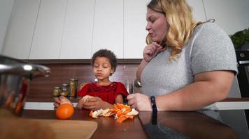ung flicka äter orange skivor och skalar Mer citrus- frukt med vuxen kvinna i en kök video