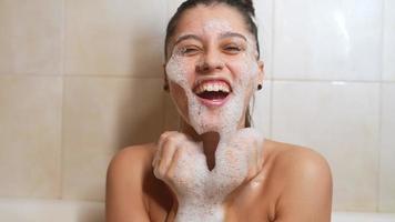 mujer joven en baño de burbujas se ríe y acaricia burbujas en la cara video