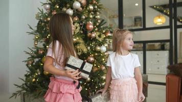 två ung flickor skratt och spela med insvept gåvor i främre av en dekorerad träd video