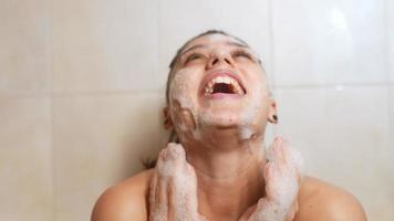 mujer joven en baño de burbujas se ríe y acaricia burbujas en el cuerpo y la cara video