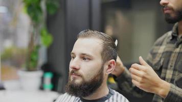 coiffeur coupe les cheveux d'un client masculin avec un peigne et une tondeuse video