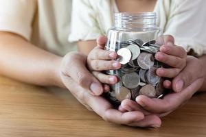 manos de adultos y niños sosteniendo un frasco de monedas concepto de ahorro y donación foto