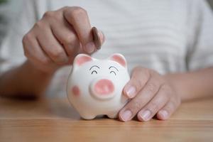 Woman hands holding and putting Thai currency coin into piggy bank. Saving concept with piggy bank at home. photo