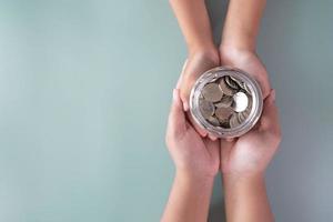 Adult and kid hands holding a coins jar savings and donation concept photo