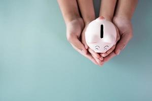 Adult and kid hands holding a piggy bank in savings concept