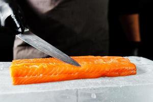 primer plano de la mano del chef preparado para cocinar filete de salmón fresco, fondo negro foto