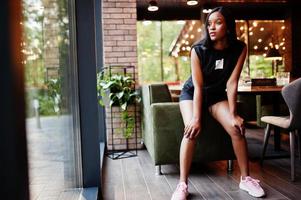 Fashionable feminist african american woman wear in black t-shirt and shorts, posed at restaurant. photo