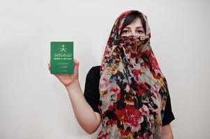 Young arabian muslim woman in hijab clothes hold Kingdom of Saudi Arabia passport on white wall background, studio portrait. photo