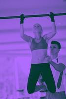 trainer support young woman while lifting on bar in fitness gym photo