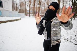 mujer musulmana africana vestida con bufanda hijab negra posa en el día de invierno en europa y muestra la señal de alto a mano. foto