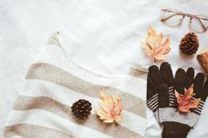 Flat lay of autumn fashion style, sweater, scarf and eyeglasses with maple leaves on white sheet background photo