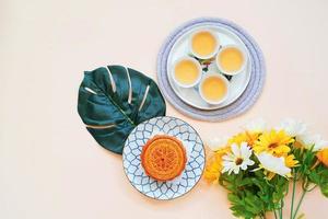 Top view of chinese moon cake with hot tea and flower on yellow background, holiday and festival concept photo