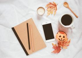 Autumn and halloween style concept, notebook and smartphone with coffee on white bed sheet background photo