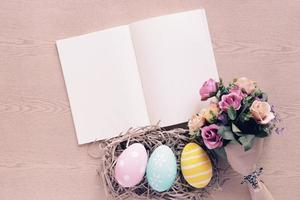 Pastel and colorful easter eggs on nest with bouquet of flower and blank book and copy space, happy easter concept photo