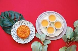 Flat lay of chinese moon cake with hot tea and green plant on red background, holiday and festival concept photo