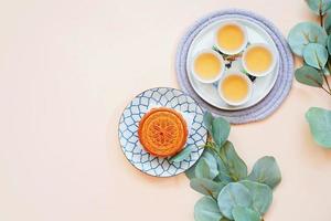 Top view of chinese moon cake with hot tea and green plant on yellow background, holiday and festival concept photo