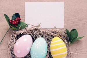 huevos de pascua en colores pastel y coloridos en nido con planta y tarjeta de felicitación en blanco y espacio para copiar, concepto de pascua feliz foto