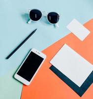 diseño plano creativo del escritorio del espacio de trabajo con teléfono inteligente, sobre, tarjeta de presentación y gafas de sol sobre un fondo de color mínimo foto