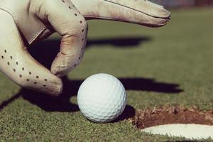 man's hand putting golf ball in hole photo