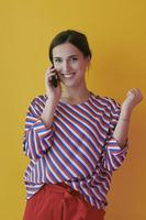 Portrait of young girl talking on the phone while standing in front of yellow background photo