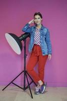 Young woman leaning against studio flashlight over a pink background photo