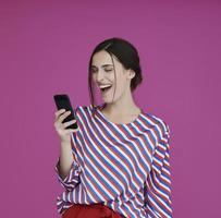 Portrait of young girl with happy face while using smartphone isolated on pink background photo