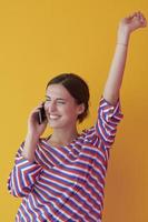 Portrait of young girl talking on the phone while standing in front of yellow background photo