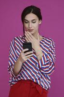 Portrait of young girl with surprised  face while using smartphone isolated on pink background photo