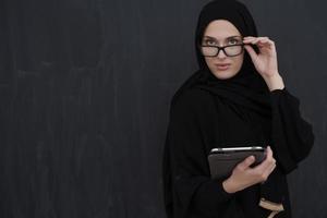 Young Arab businesswoman in traditional clothes or abaya holding tablet computer photo