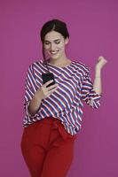 Portrait of young girl with happy face while using smartphone isolated on pink background photo