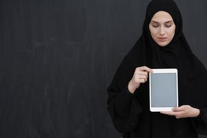 Young Arab businesswoman in traditional clothes or abaya holding tablet computer photo