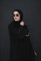 Young muslim in traditional clothes or abaya and sunglasses posing in front of black chalkboard photo