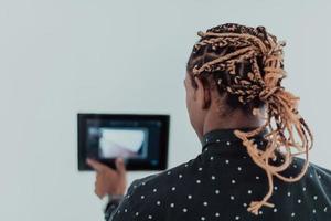 Smiling African American man using modern smart home system, controller on wall, positive young man switching temperature on thermostat or activating security alarm in apartment photo