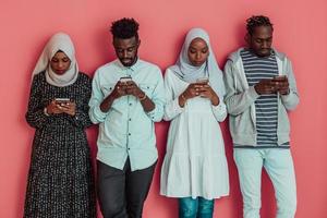 A group of African Muslim students use smartphones while standing in front of a pink background photo