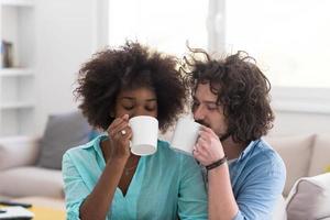 pareja multiétnica sentada en un sofá en casa bebiendo café foto