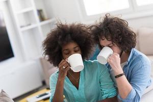 multiethnic couple sitting on sofa at home drinking coffe photo