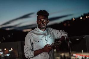 el joven en una calle urbana de la ciudad por la noche enviando mensajes de texto en un teléfono inteligente con bokeh y luces de neón en el fondo. foto