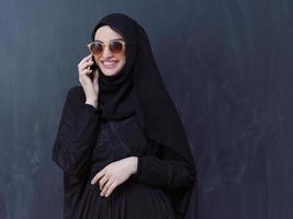 young muslim woman wearing sunglasses using smartphone photo