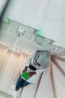 Young african modern muslim woman using tablet computer while sitting on the stairs at home wearing hijab clothes top view photo