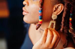 Face portrait of lovely african american woman with dreadlocks show her earrings. Beautiful cool fashionable black young girl indoor. photo