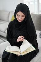 Portrait of young muslim woman reading Quran in modern home photo