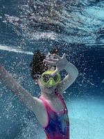 un niño sonriente con gafas nada, se sumerge en la piscina con diversión, salta profundamente bajo el agua. estilo de vida saludable, actividad de deportes acuáticos en los veranos. foto